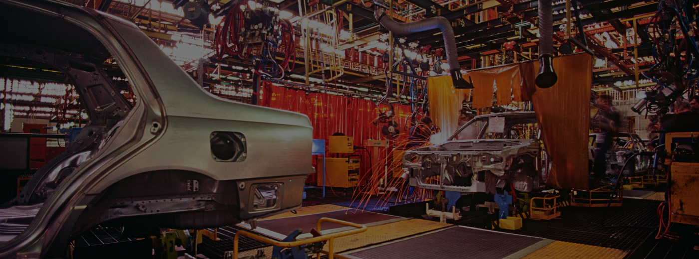 A mechanic works on a car inside a factory, surrounded by tools and equipment
