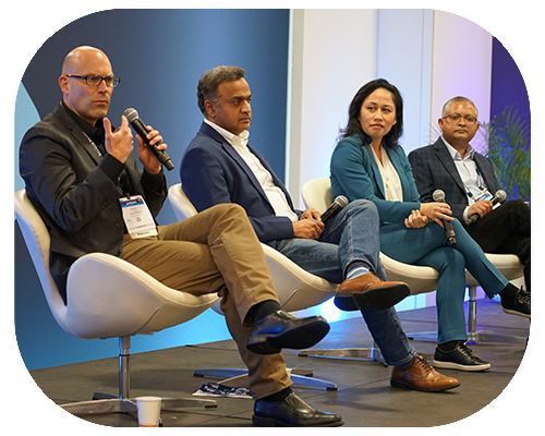 Four people sit on stage in modern chairs, each holding a microphone, participating in a panel discussion at MD&M West conference