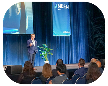 A man presenting at a conference, standing at a podium with a projector screen in the background