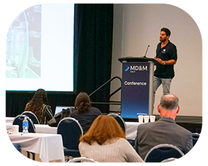 A man presenting at a conference, standing at a podium with a projector screen in the background photo