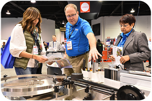 A man and woman stand together in front of a large machine, discussing its features and functionality