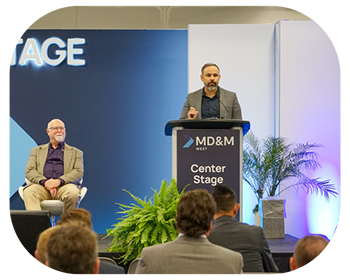 Two men sitting at a podium, preparing to speak on stage in front of attendees